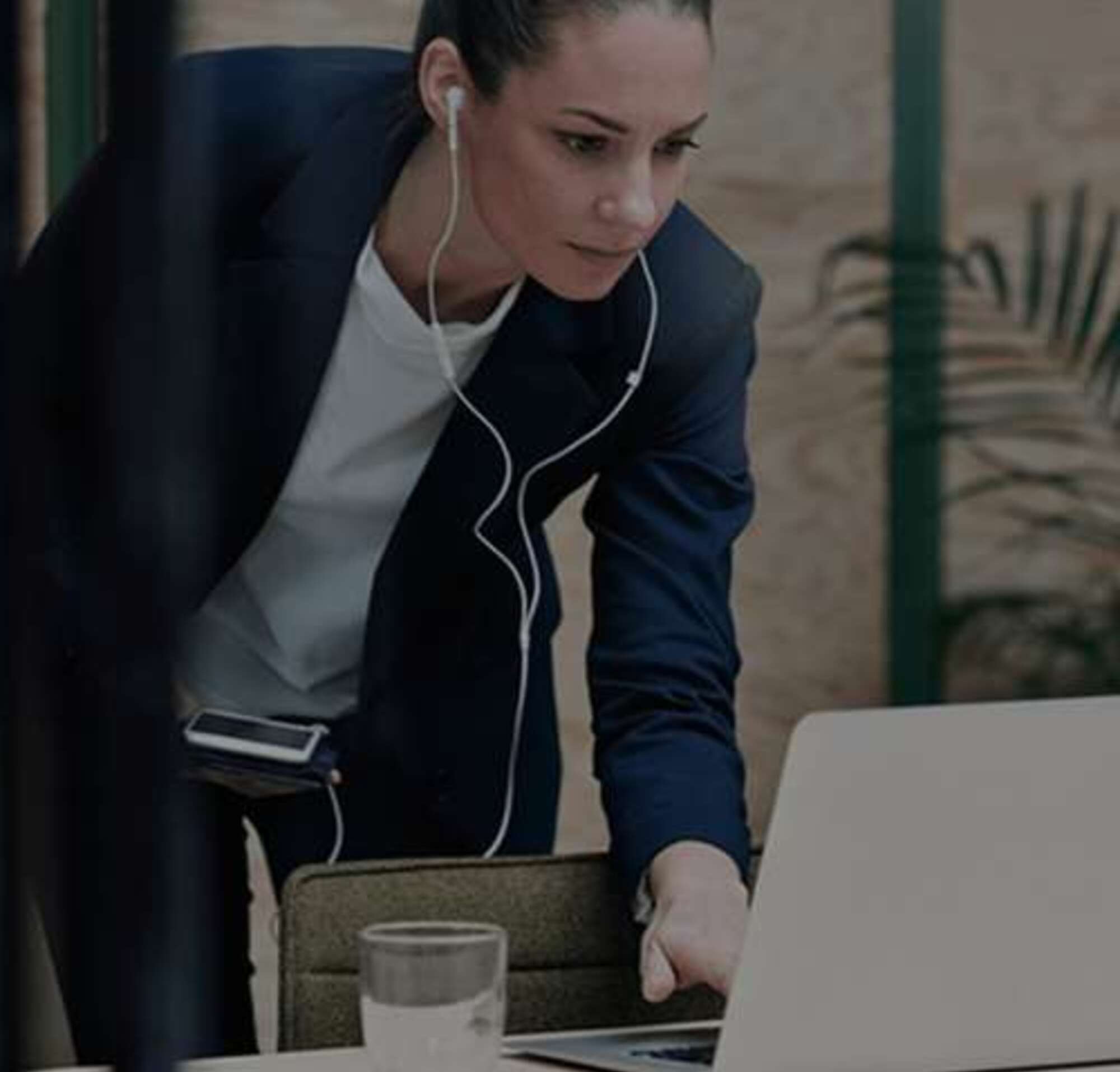 Woman with earbuds working on a laptop and holding her phone.